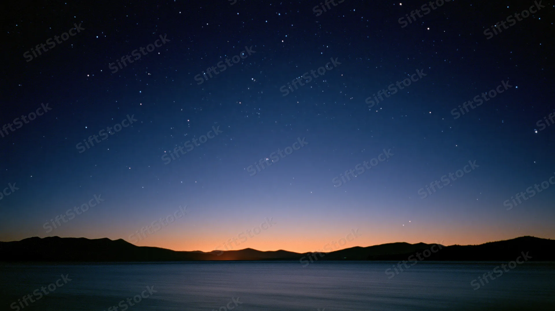 Starry night sky over calm lake with silhouetted mountains at twilight