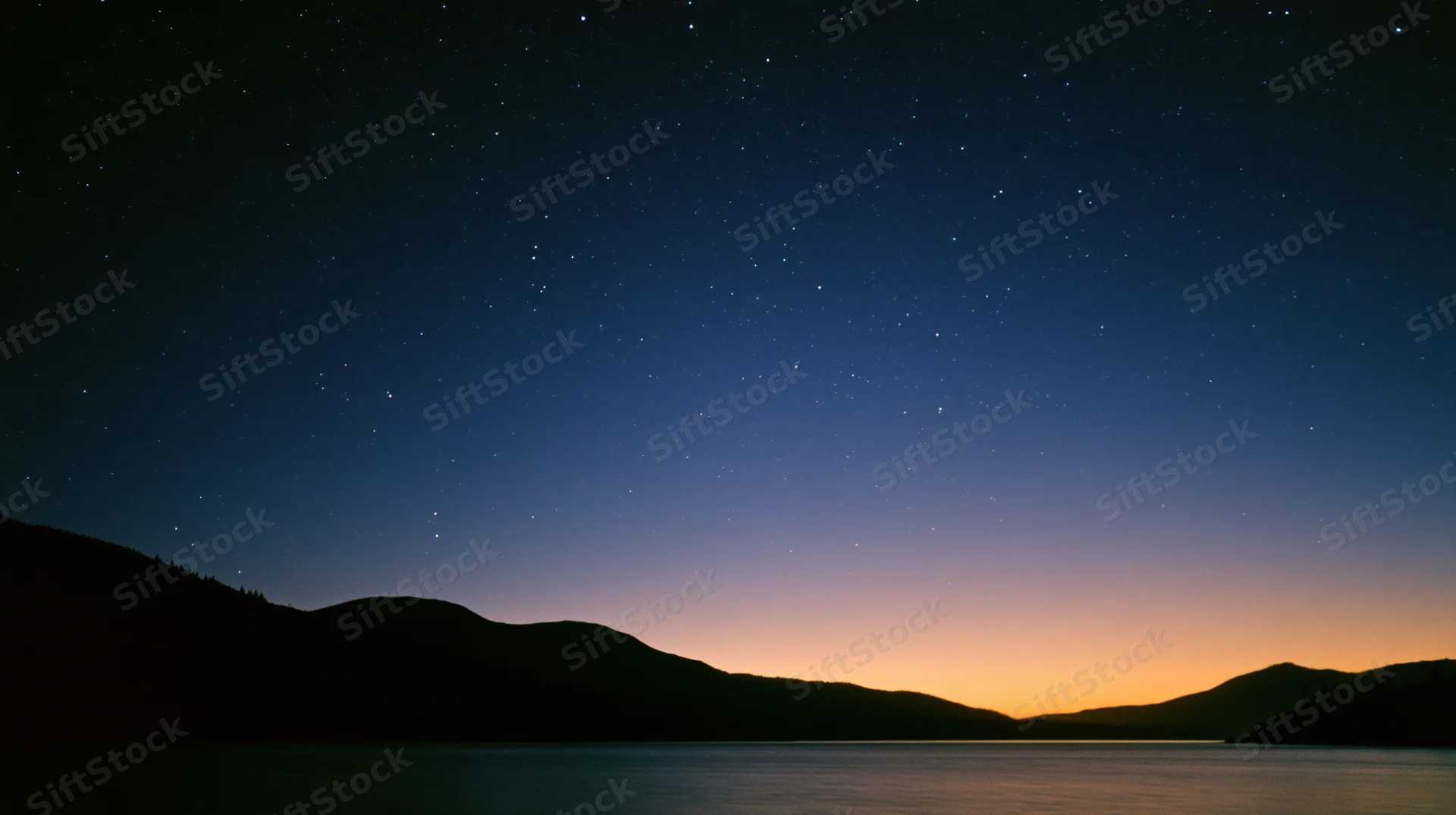 Starry night sky over calm lake with mountain silhouette at twilight