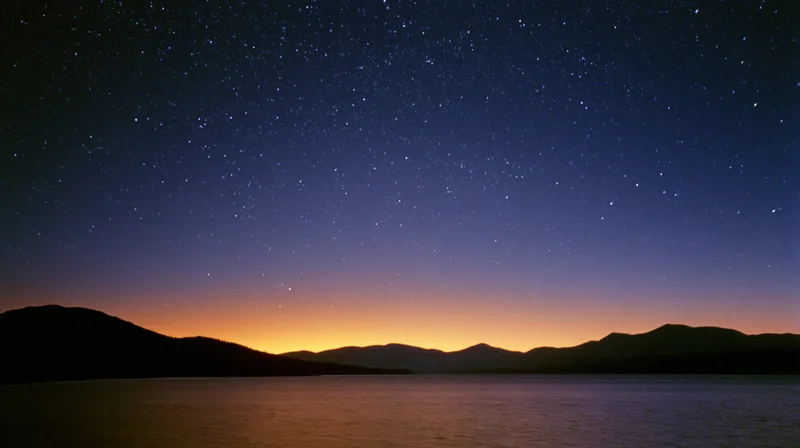 Starry night sky over calm lake with mountain silhouette at twilight