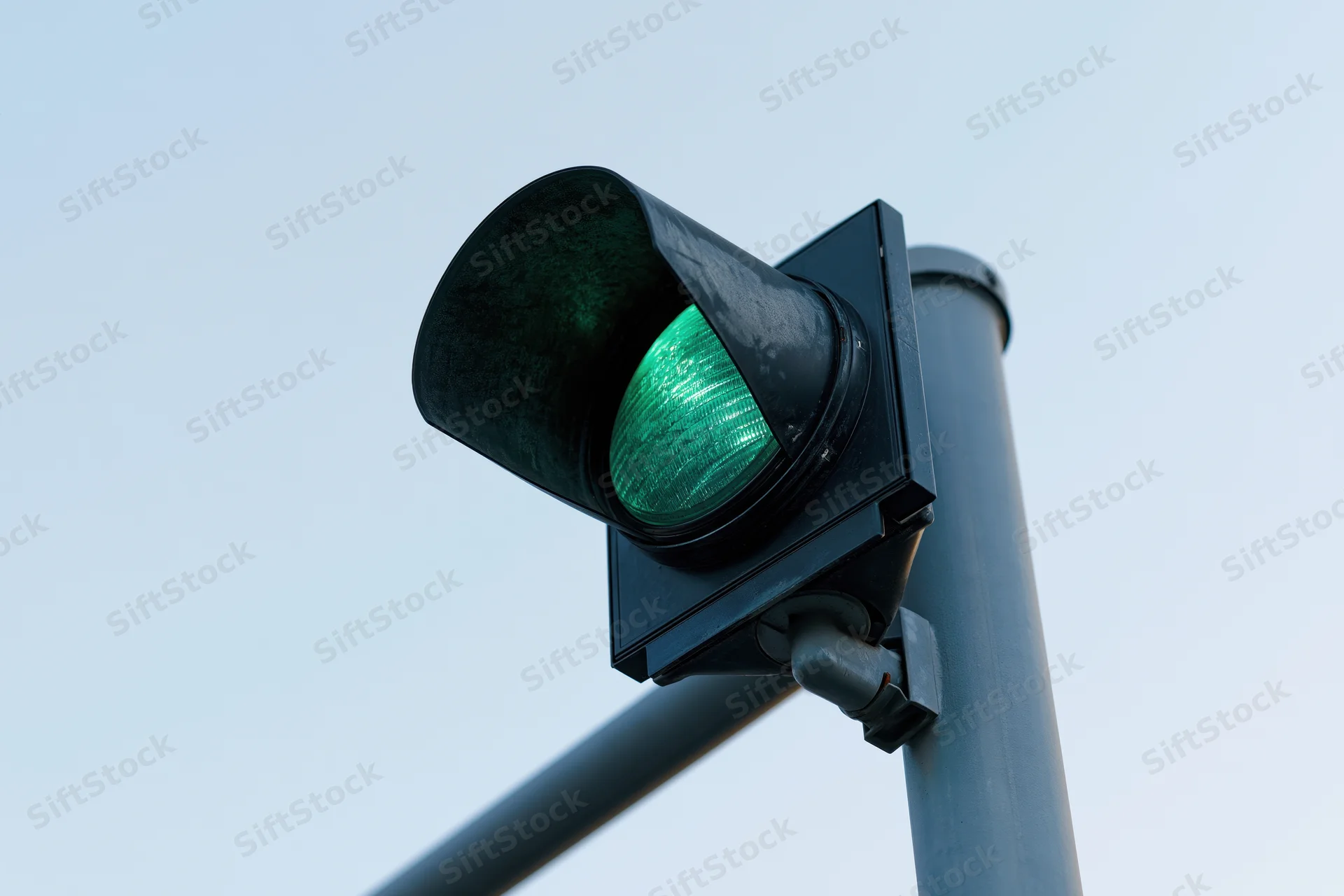 Green traffic light illuminated on steel pole against clear sky