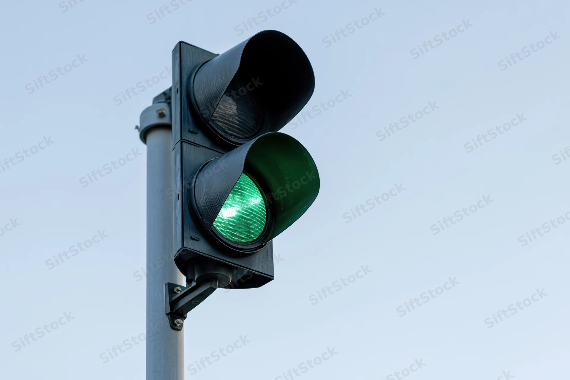 Black metal traffic light with green signal illuminated on steel pole against clear sky