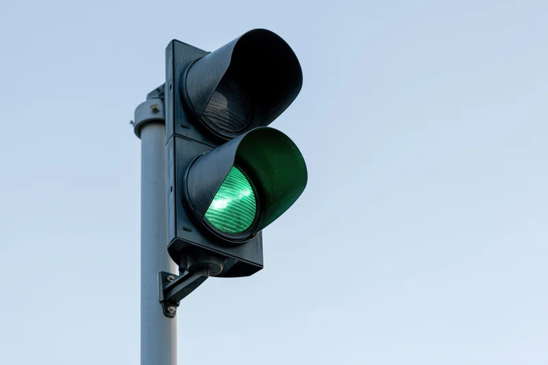 Black metal traffic light with green signal illuminated on steel pole against clear sky