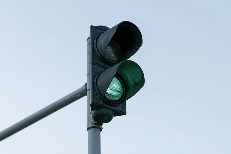 Green traffic light illuminated on steel pole against clear sky