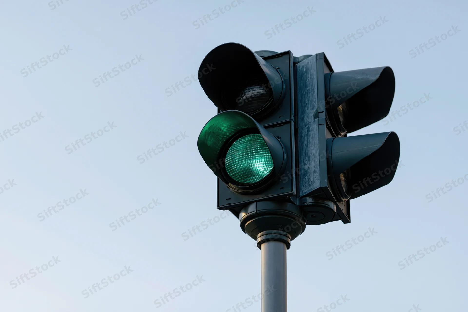 Black metal traffic light with green signal illuminated on steel pole against clear sky