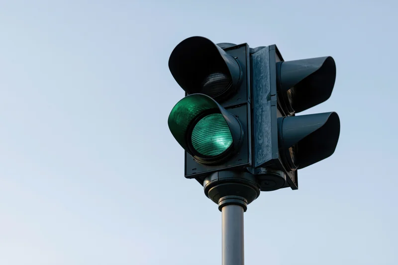 Black metal traffic light with green signal illuminated on steel pole against clear sky