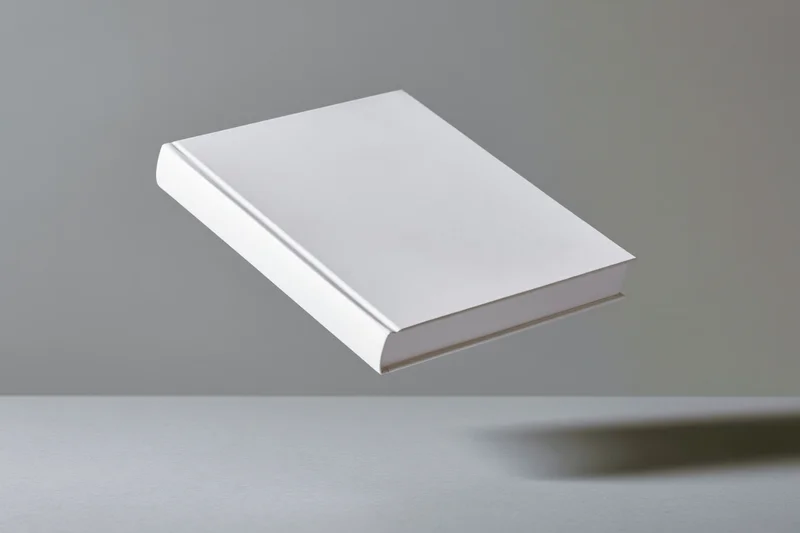 Blank white hardcover book floating above gray surface in studio setting