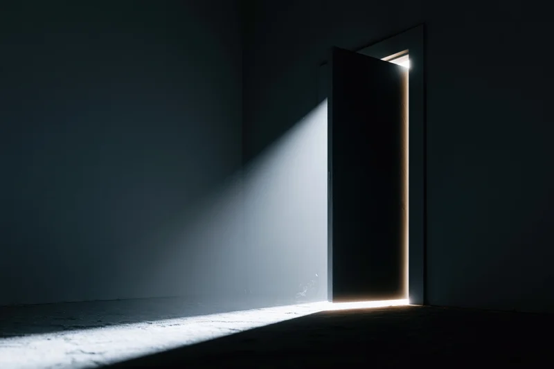 Slightly open door in dark room letting in bright white light