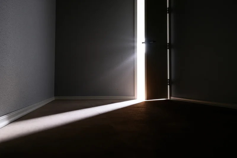 Slightly open door letting bright sunlight into dark empty room