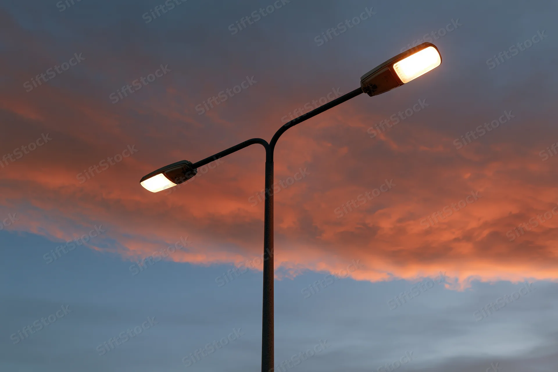 Dual-arm led street lamp pole illuminated against twilight sky with orange and blue clouds