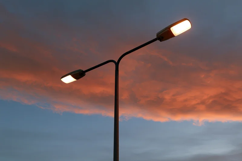 Dual-arm led street lamp pole illuminated against twilight sky with orange and blue clouds
