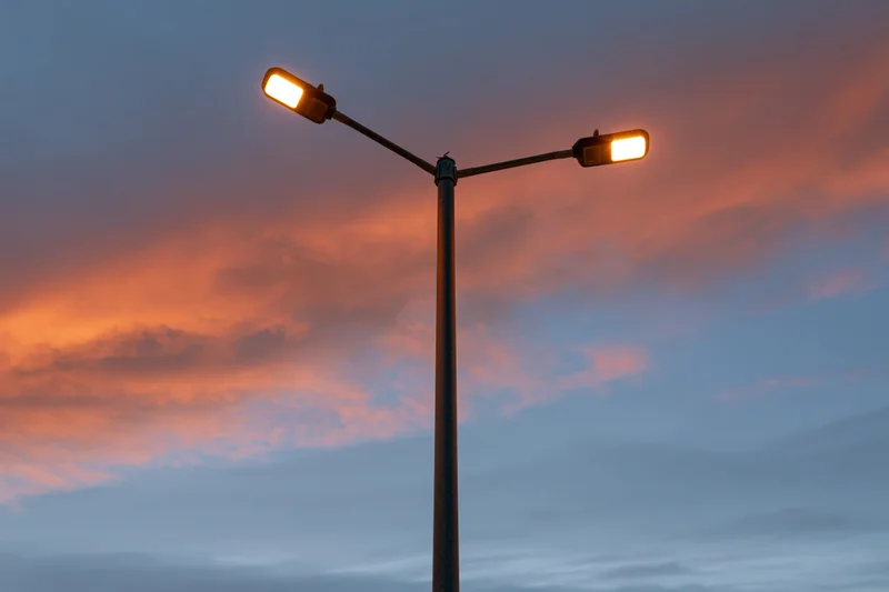 Dual-arm led street lamp pole illuminated against twilight sky with orange and pink clouds