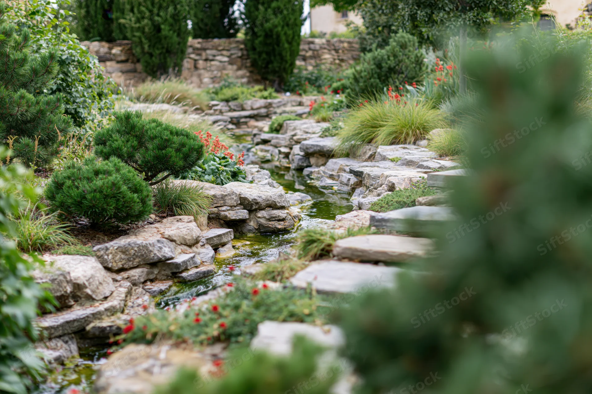 A landscaped garden with a small natural stone stream winding through greenery and flowering plants