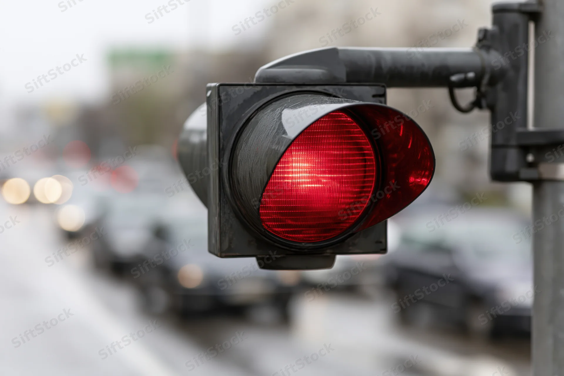 Red traffic light illuminated on a metal arm above a city street with blurred vehicles in the background
