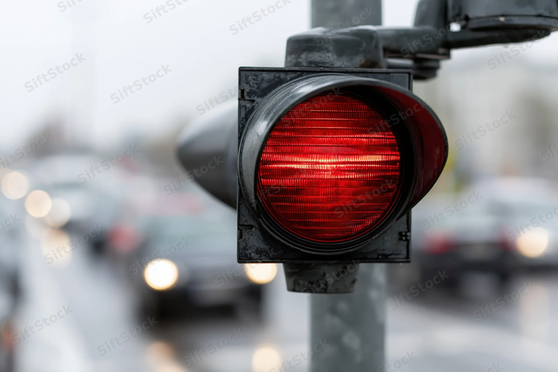 Red traffic light illuminated on a metal pole above a busy street with blurred vehicles in the background