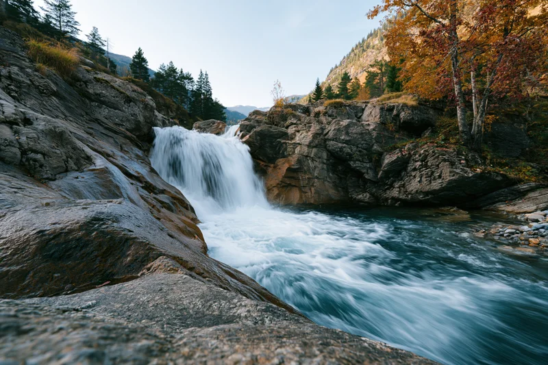 Waterfall cascading over granite ledges into a rushing river surrounded by autumn forest
