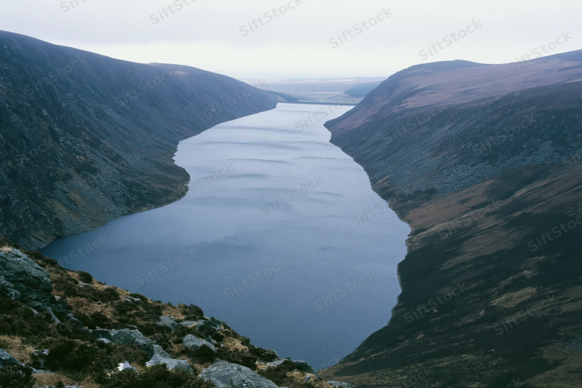 Narrow mountain reservoir winding through deep valley with rocky slopes and calm water surface