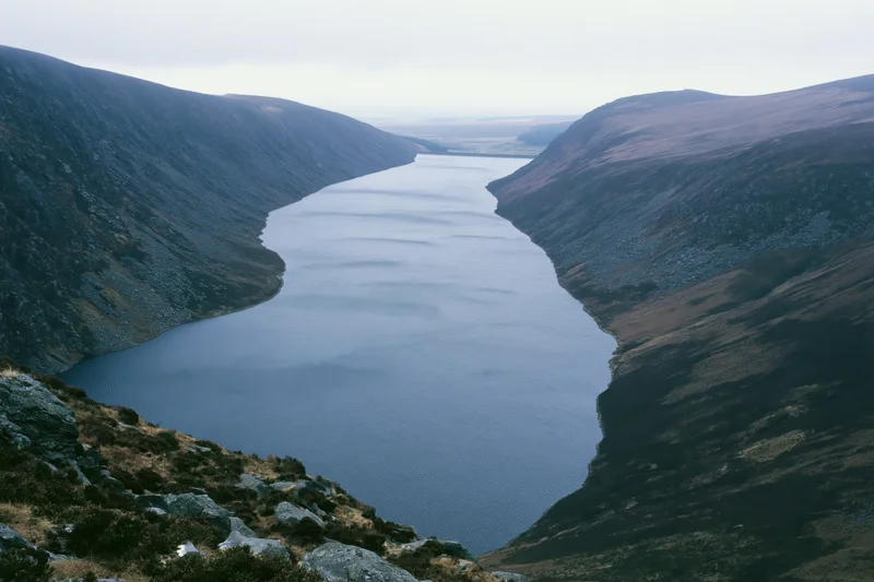 Narrow mountain reservoir winding through deep valley with rocky slopes and calm water surface