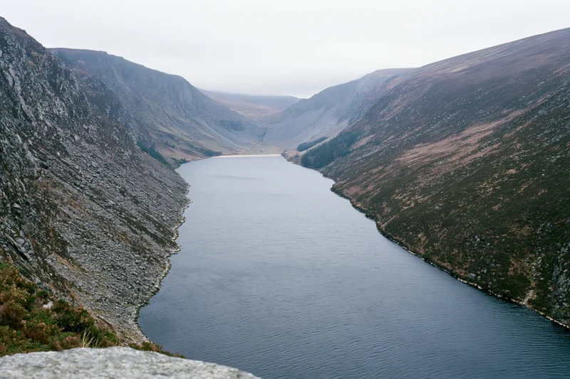 Narrow mountain reservoir stretching into deep valley surrounded by rocky slopes and sparse vegetation