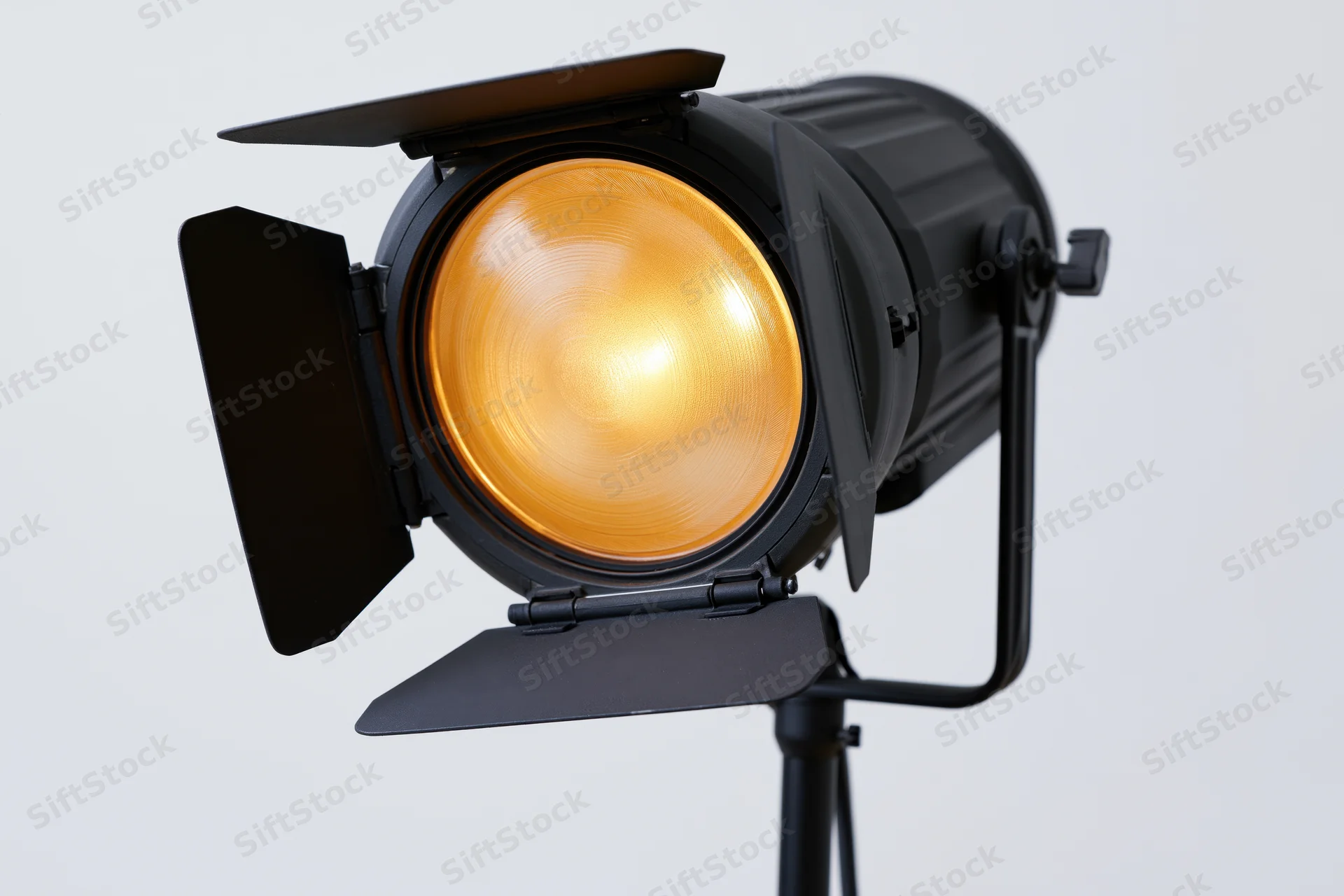 Professional studio strobe light with barn doors open on a stand, emitting warm glow