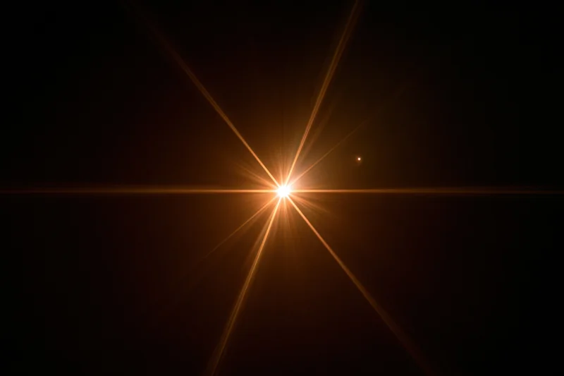 Bright point of light radiating golden beams against dark background