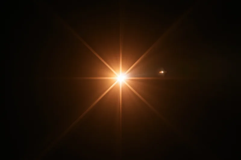 Bright point of light creating starburst flare against dark background