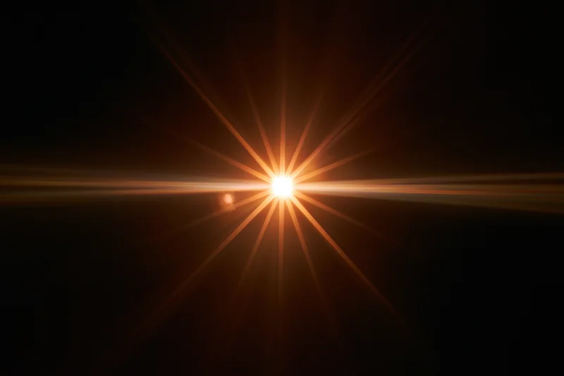 Bright point of light bursting with starburst flare against black background