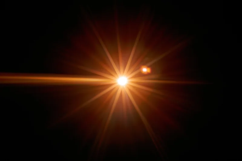 Bright point of light bursting with starburst flare against black background