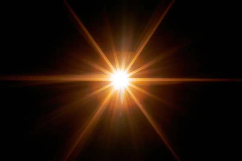 Bright point of light emitting radial lens flare against black background