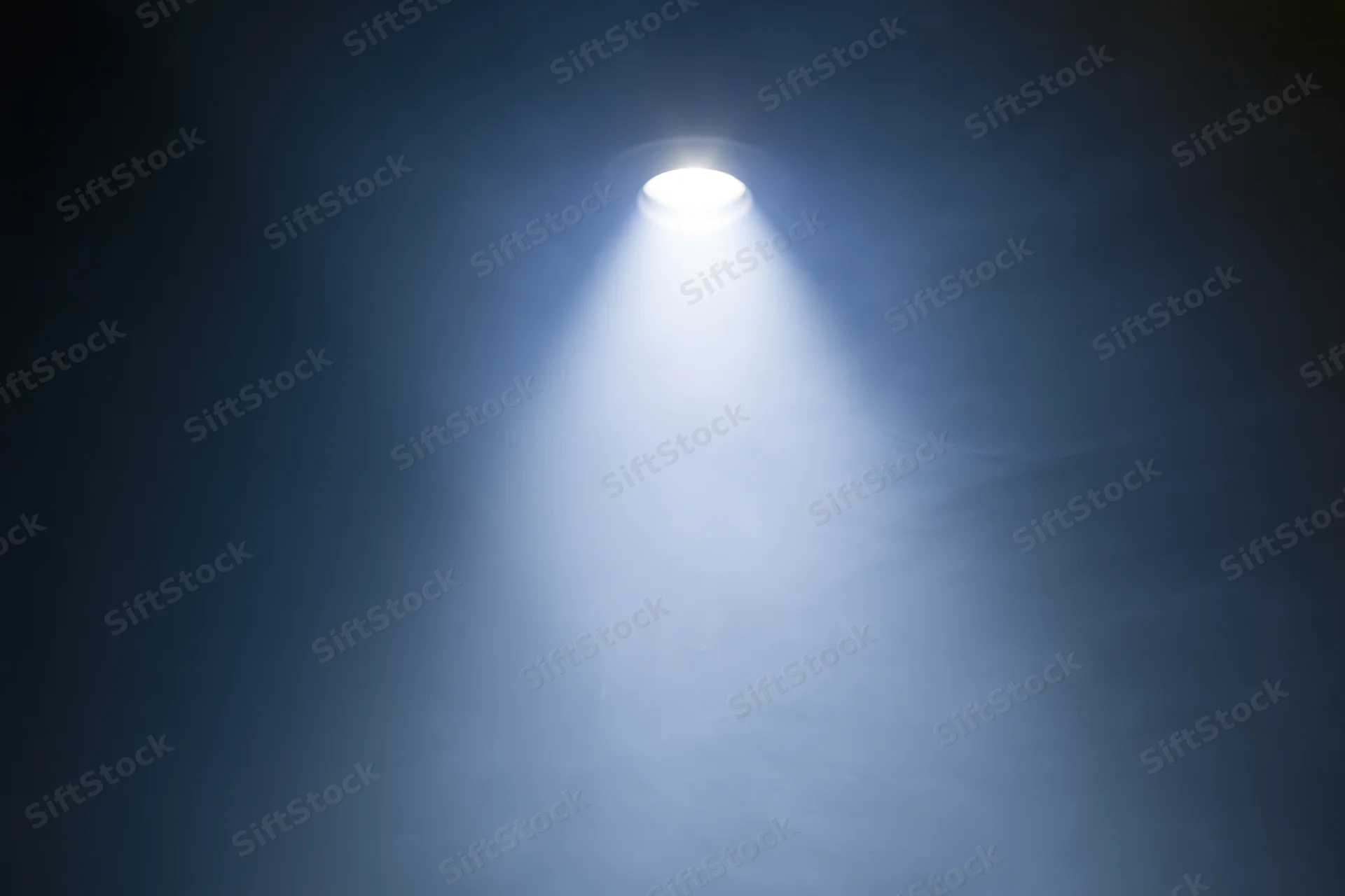 Single spotlight casting bright white beam upward in dark smoky space