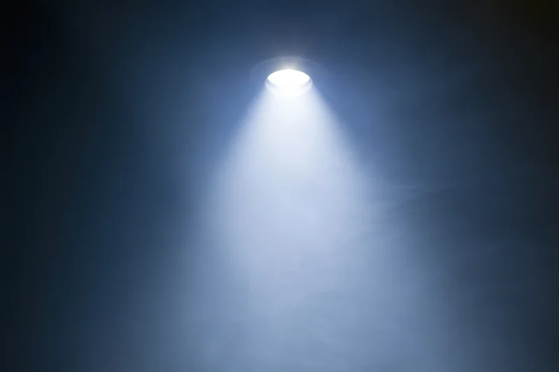 Single spotlight casting bright white beam upward in dark smoky space