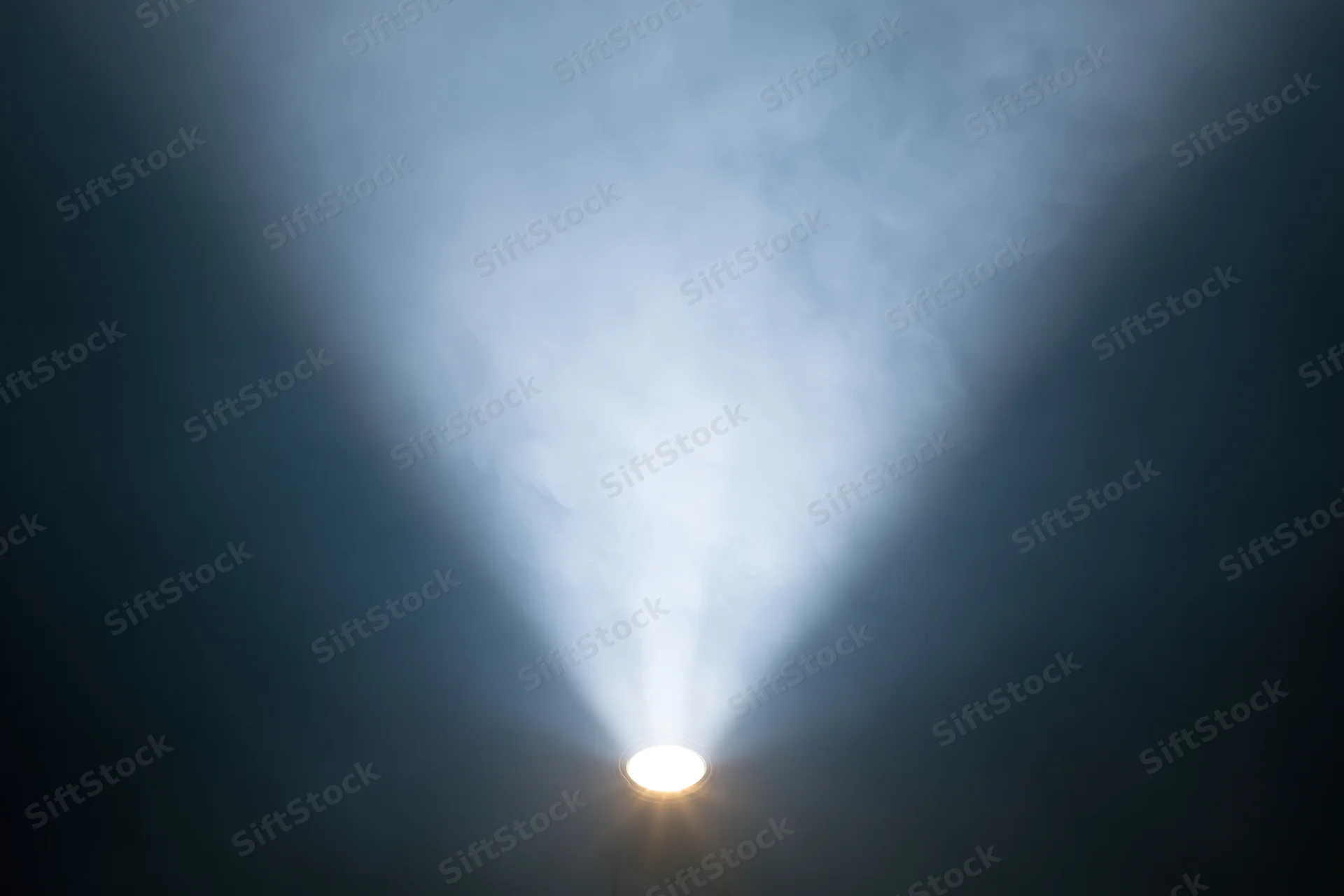 Single spotlight projecting upward beam through smoke in dark space