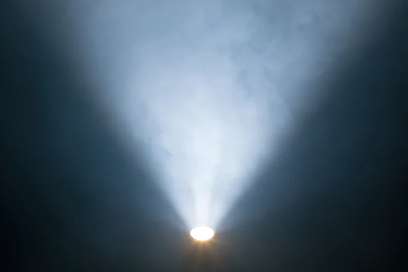 Single spotlight projecting upward beam through smoke in dark space