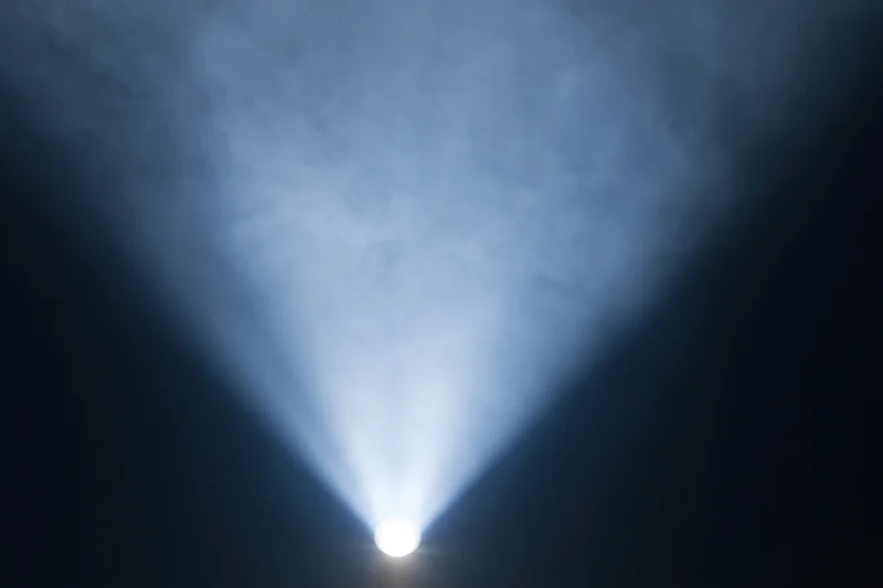 Bright white spotlight beam projecting upward into dark smoky air