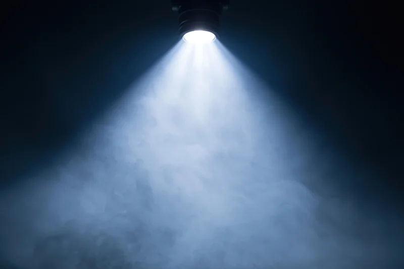 Spotlight beam cutting through smoke in dark theater ceiling