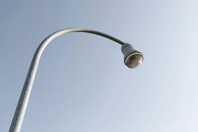 Curved metal streetlight pole against clear blue sky from low angle view