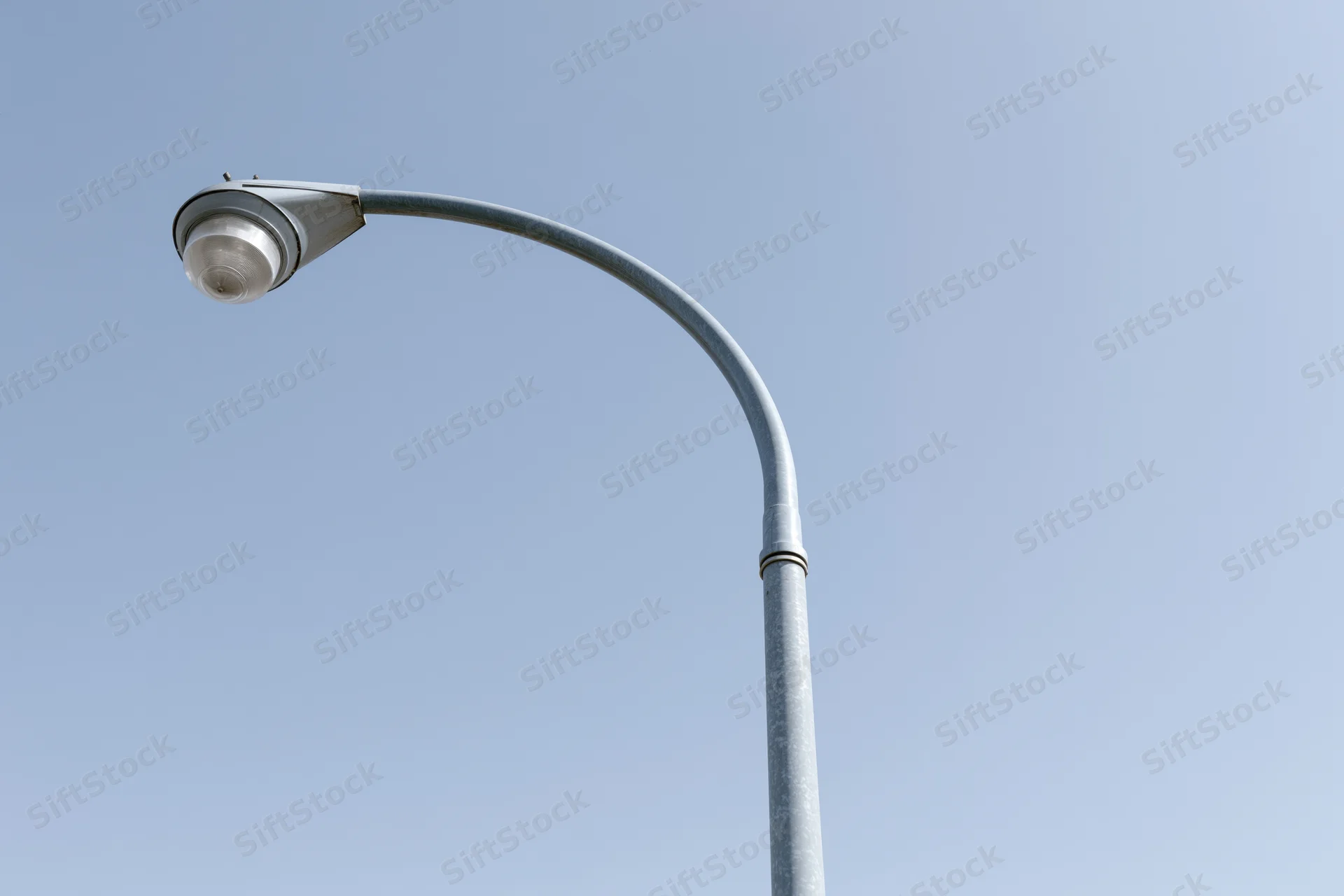 Curved metal street lamp pole against clear blue sky from low angle