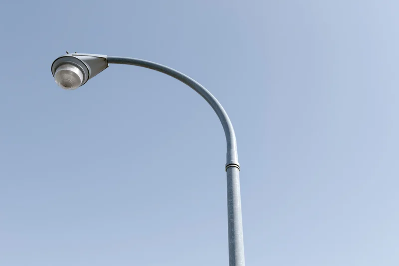 Curved metal street lamp pole against clear blue sky from low angle
