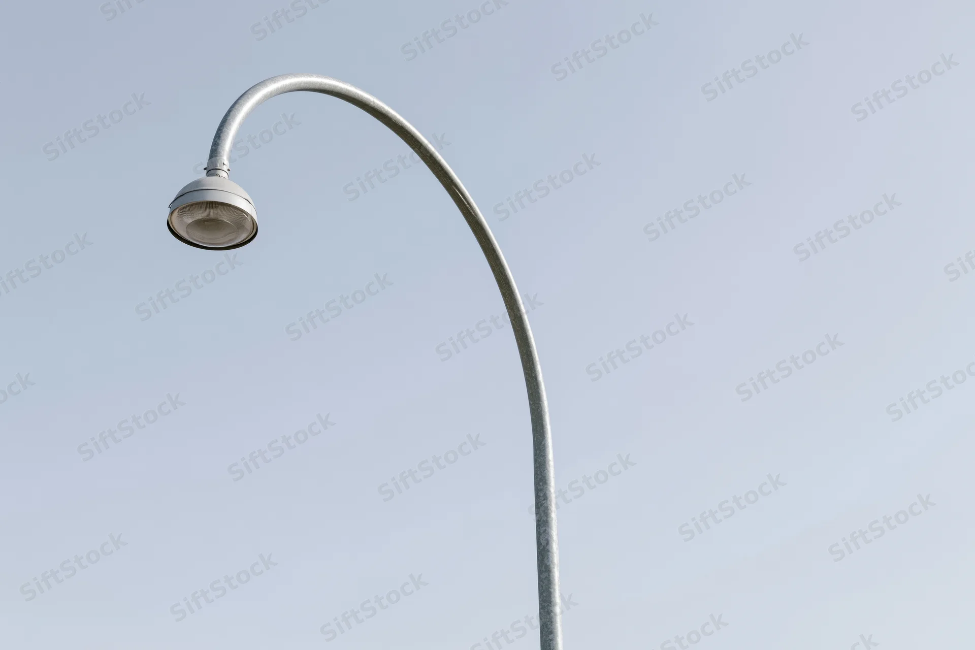 Curved metal street lamp pole against clear sky with copyspace