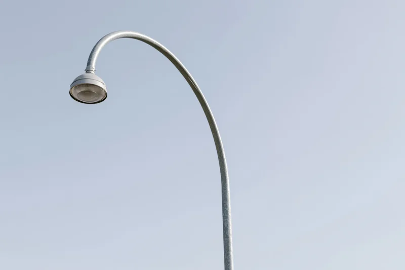 Curved metal street lamp pole against clear sky with copyspace