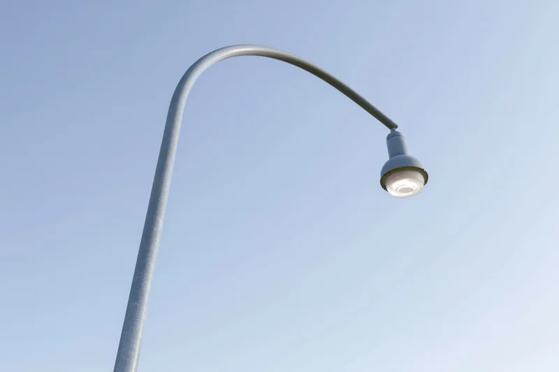 Curved metal street lamp pole viewed from below against clear blue sky