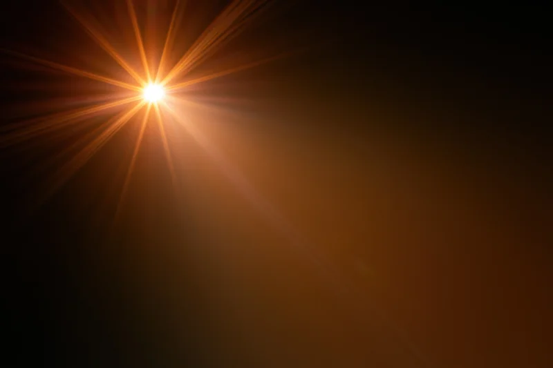 Intense light source bursting from upper left corner against dark background with radiating beams and warm glow