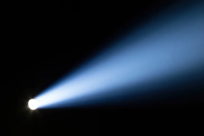 Intense spotlight beam cutting diagonally across dark background
