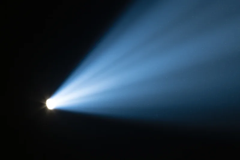 Intense spotlight beam cutting diagonally across dark background