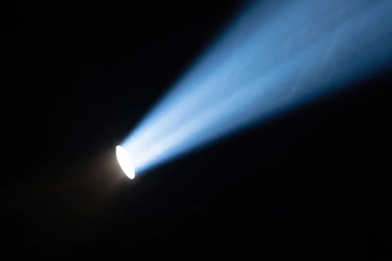 Intense spotlight beam cutting diagonally across dark background