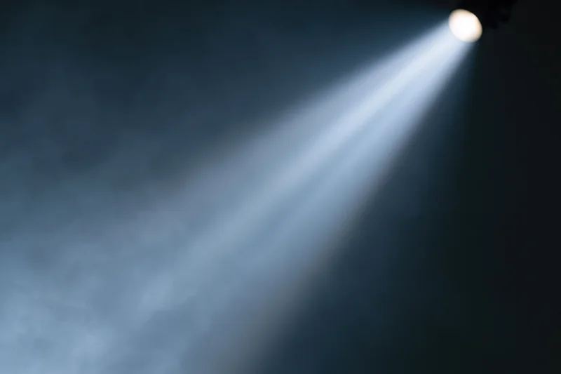 Single spotlight beam cutting diagonally through haze in a dark theater space