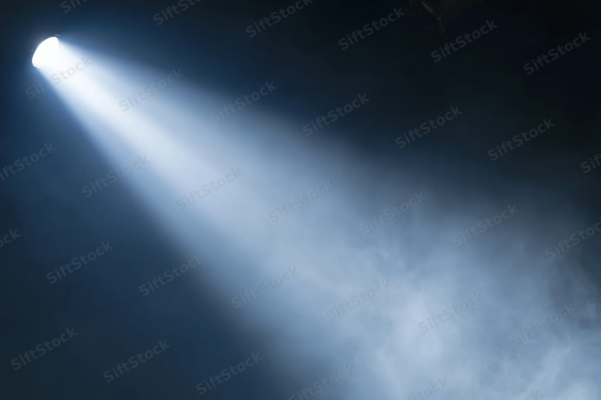 Single spotlight beam cutting diagonally through haze in dark theater space