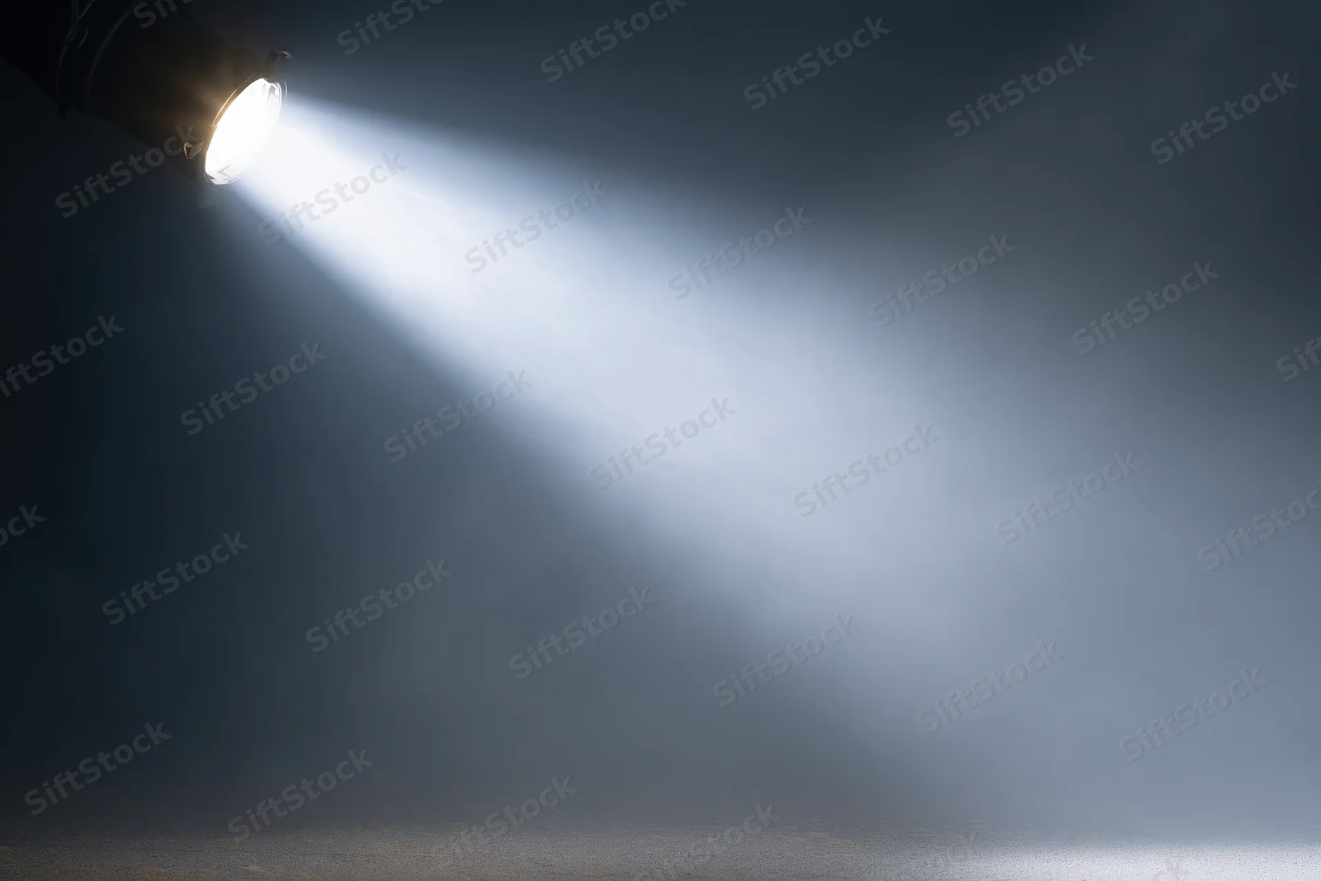 Single spotlight mounted in upper left casting a sharp beam of light across a dark smoky stage space