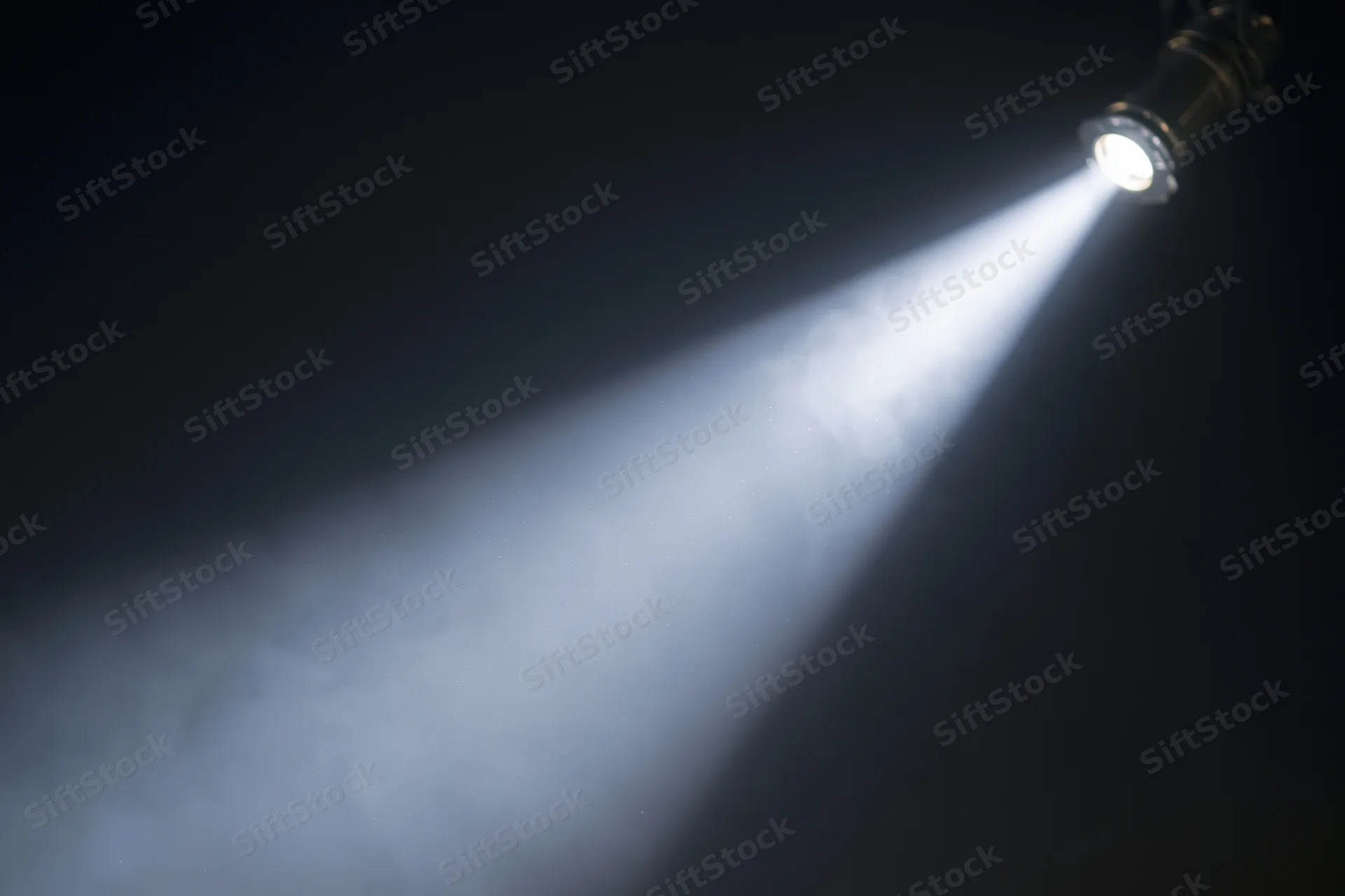Single spotlight casting a sharp beam of light through smoke in a dark theater setting