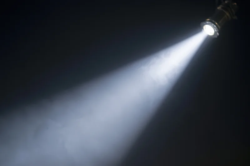 Single spotlight casting a sharp beam of light through smoke in a dark theater setting