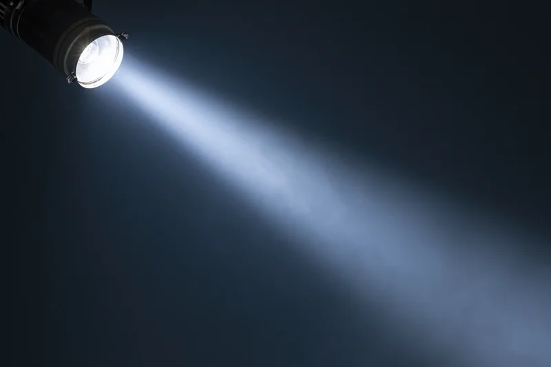 Single spotlight mounted on ceiling casting bright beam across dark space